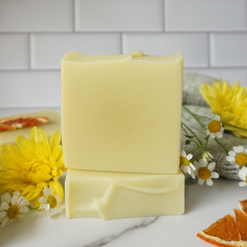 Yellow soap bars with flowers and orange slices on a white marble surface with a tiled wall background.