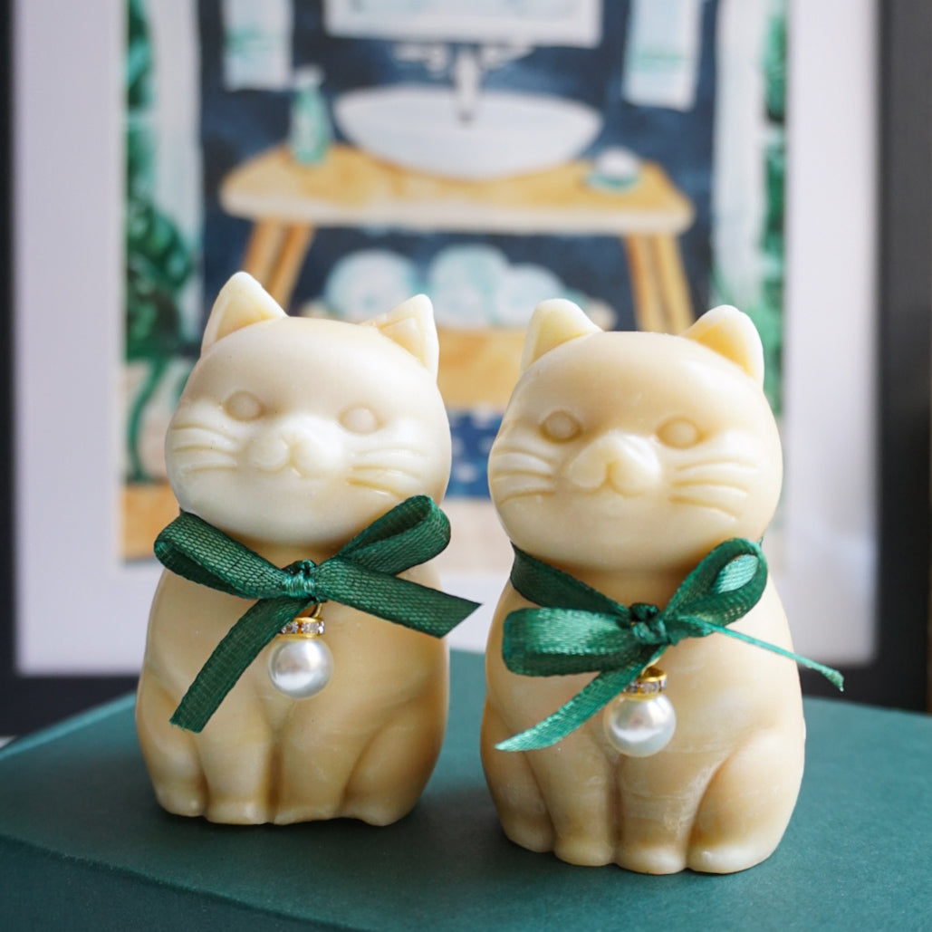 Two cat-shaped soap figurines with green ribbons on a teal surface.