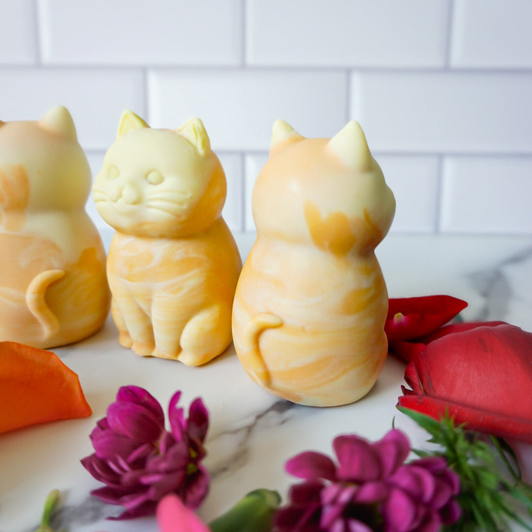 Three cat-shaped soap bars on a marble surface with flowers around