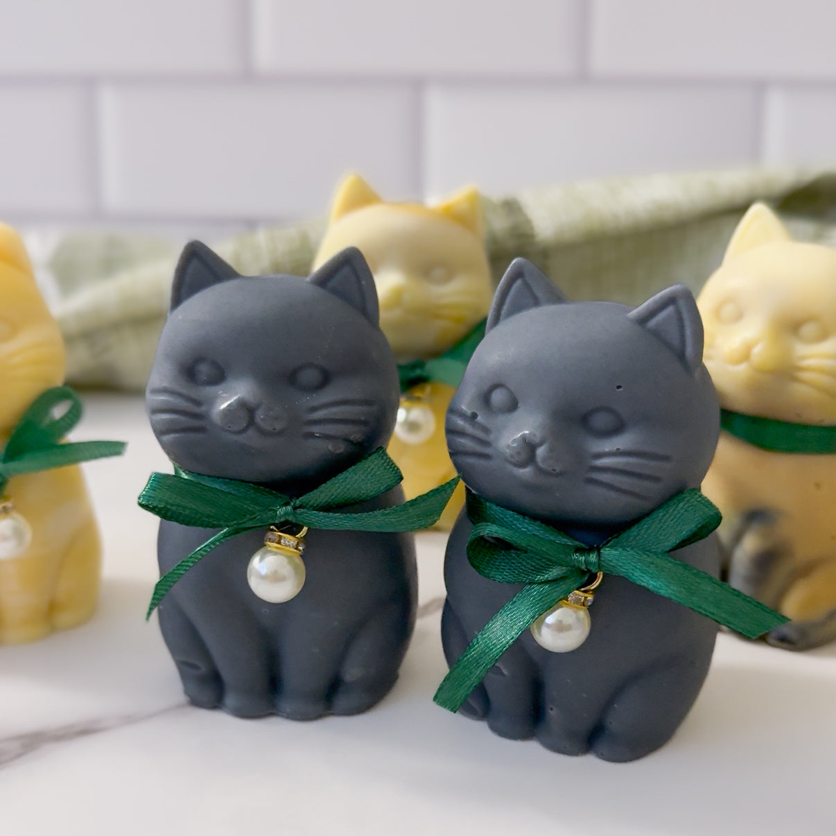 Two gray cat-shaped soaps with green ribbons and pearl decorations on a white surface.