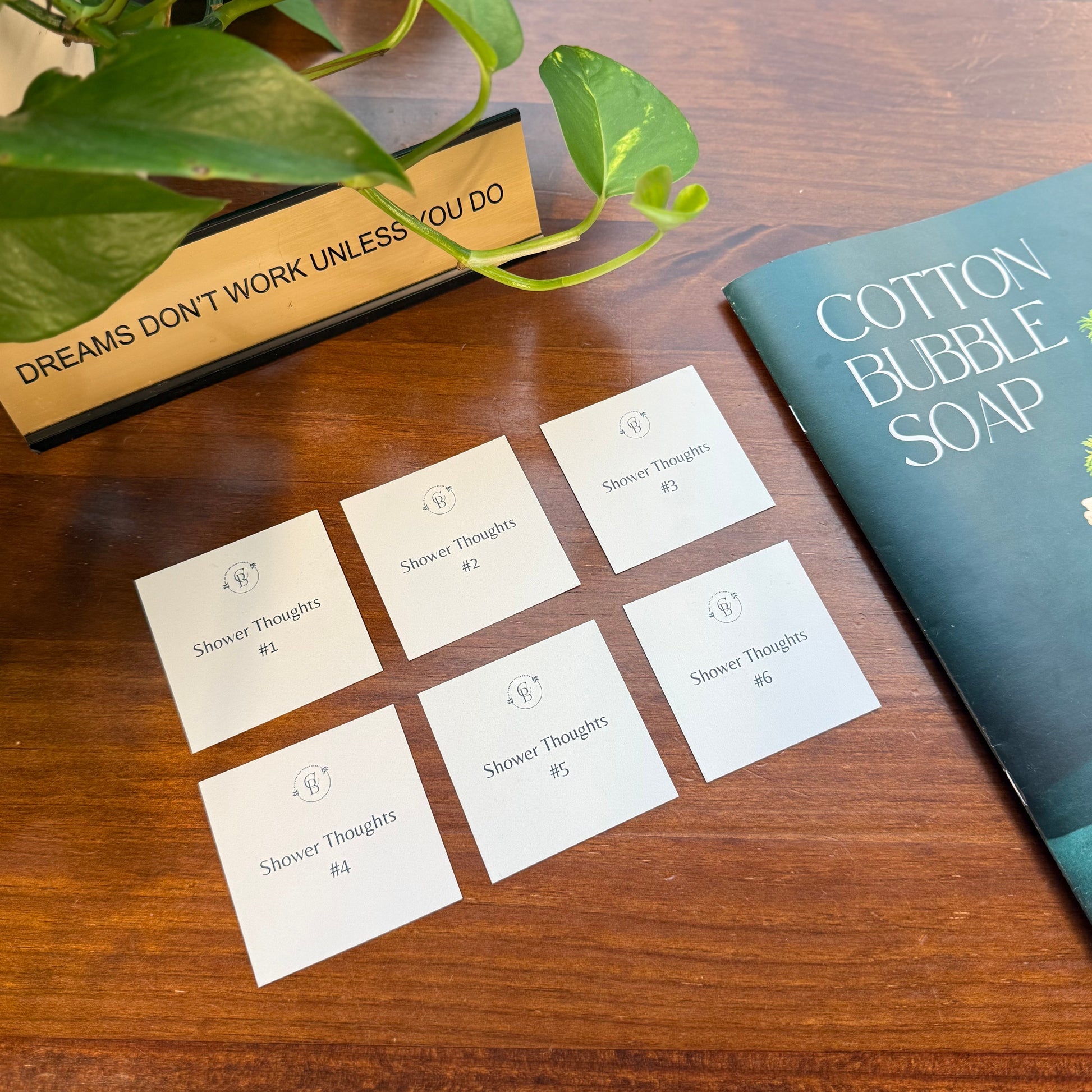 Set of cards labeled 'Shower Thoughts' on a wooden surface with a plant and book in the background.