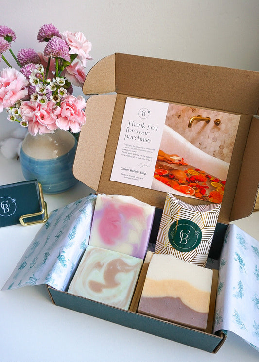 Open box containing soap bars and a card with floral decorations on a white surface.