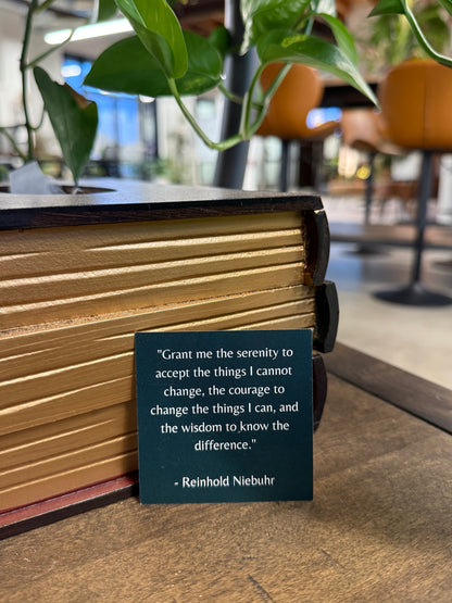 Book with a quote card on a wooden surface, surrounded by plants