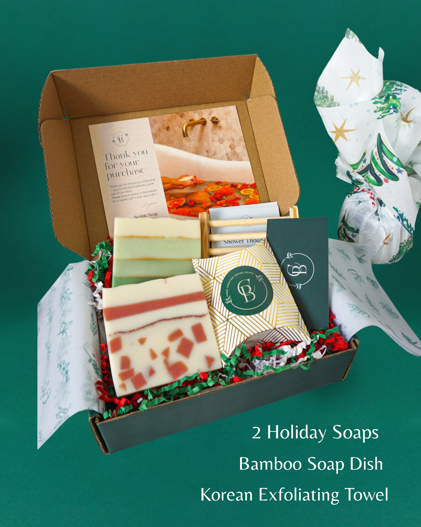 Gift set with holiday soaps, bamboo soap dish, and Korean exfoliating towel on a green background.