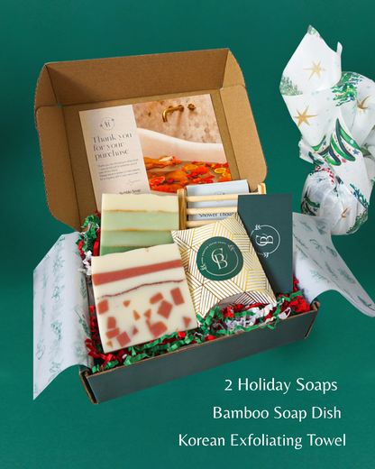 Gift set with holiday soaps, bamboo soap dish, and Korean exfoliating towel on a green background.