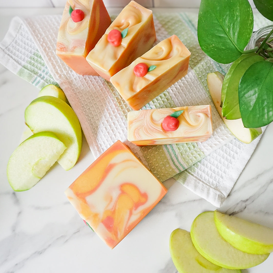 Handmade soap bars with apple slices and leaves on a marble surface