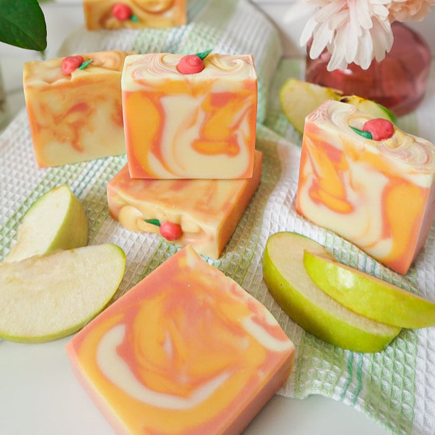 Decorative soap bars with apple slices and flowers on a white surface
