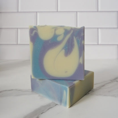 Two swirled soap bars stacked on a marble surface with a white tiled wall background