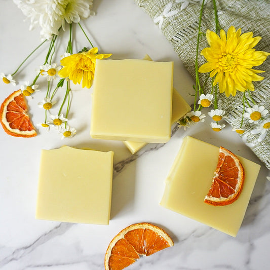 Three yellow soap bars on a marble surface with orange slices and flowers.