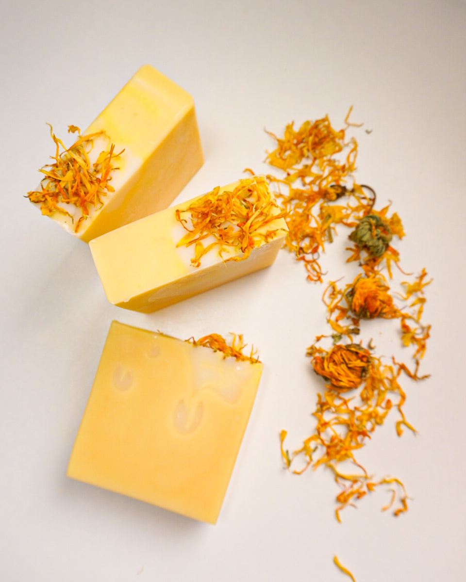 Three yellow soap bars with calendula flowers on a light gray background