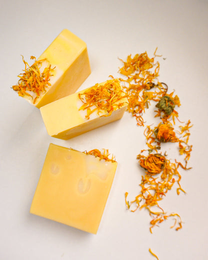 Three yellow soap bars with calendula flowers on a light gray background