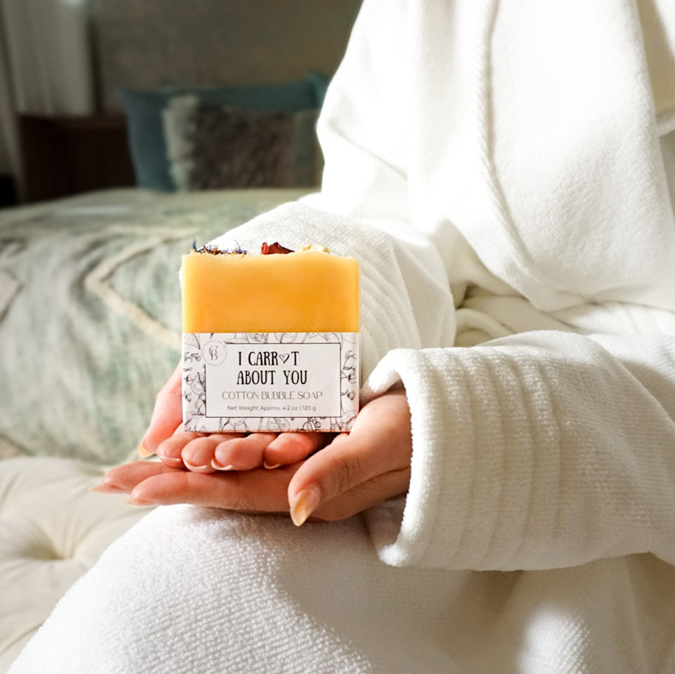 Person holding a bar of soap with 'I Care About You' text in a cozy bathrobe.