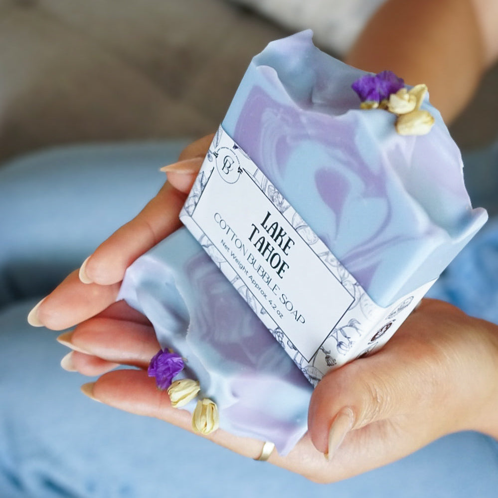 Hand holding a purple soap bar with decorative elements and a label.