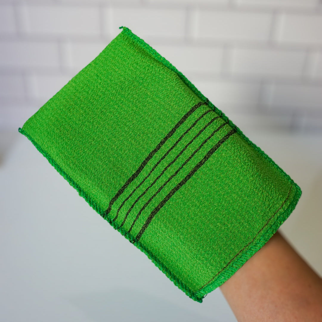 Green bath towel with black stripes held by a person against a white tiled wall.