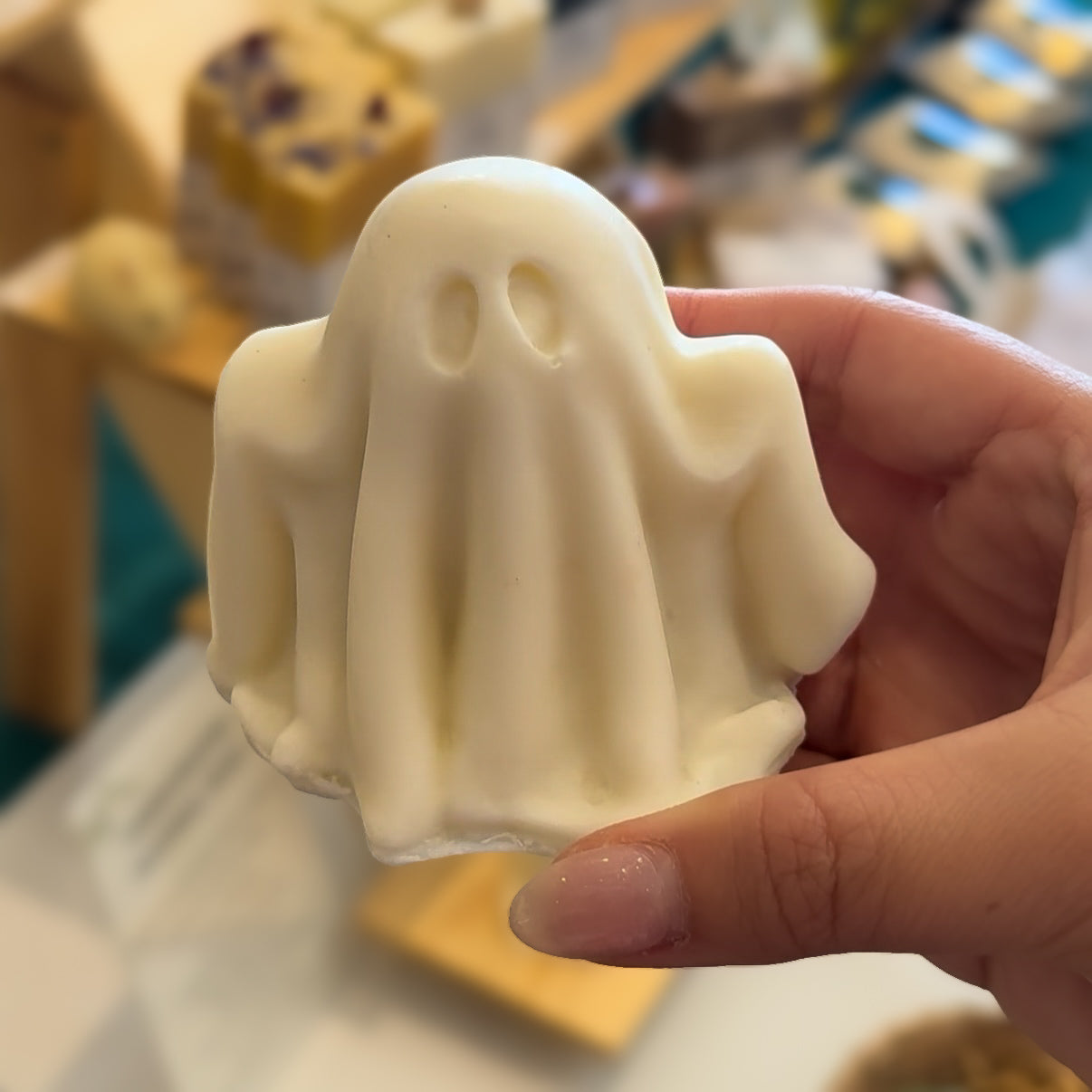 Hand holding a white ghost-shaped soap with a blurred background