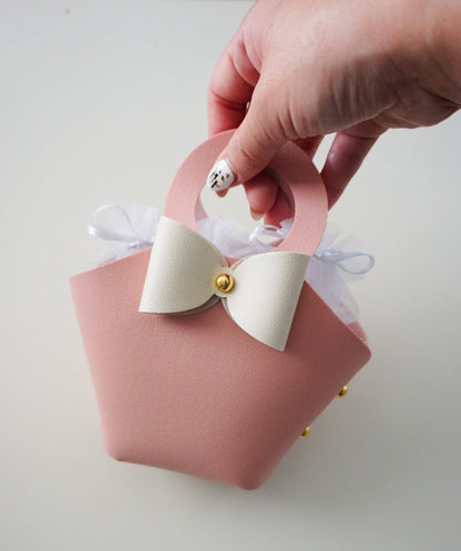 Pink gift bag with a white bow held by a hand on a light gray background