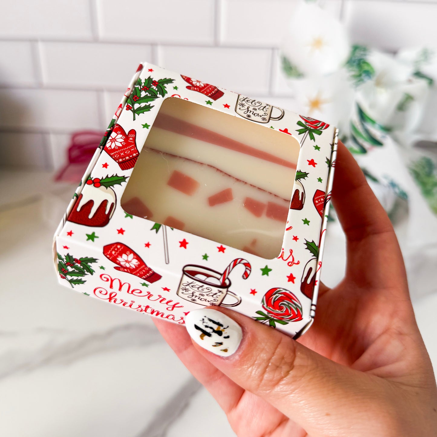 Hand holding a Christmas-themed soap packaging with visible soap inside.
