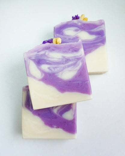 Three bars of purple and white soap on a light gray background with cotton flowers.