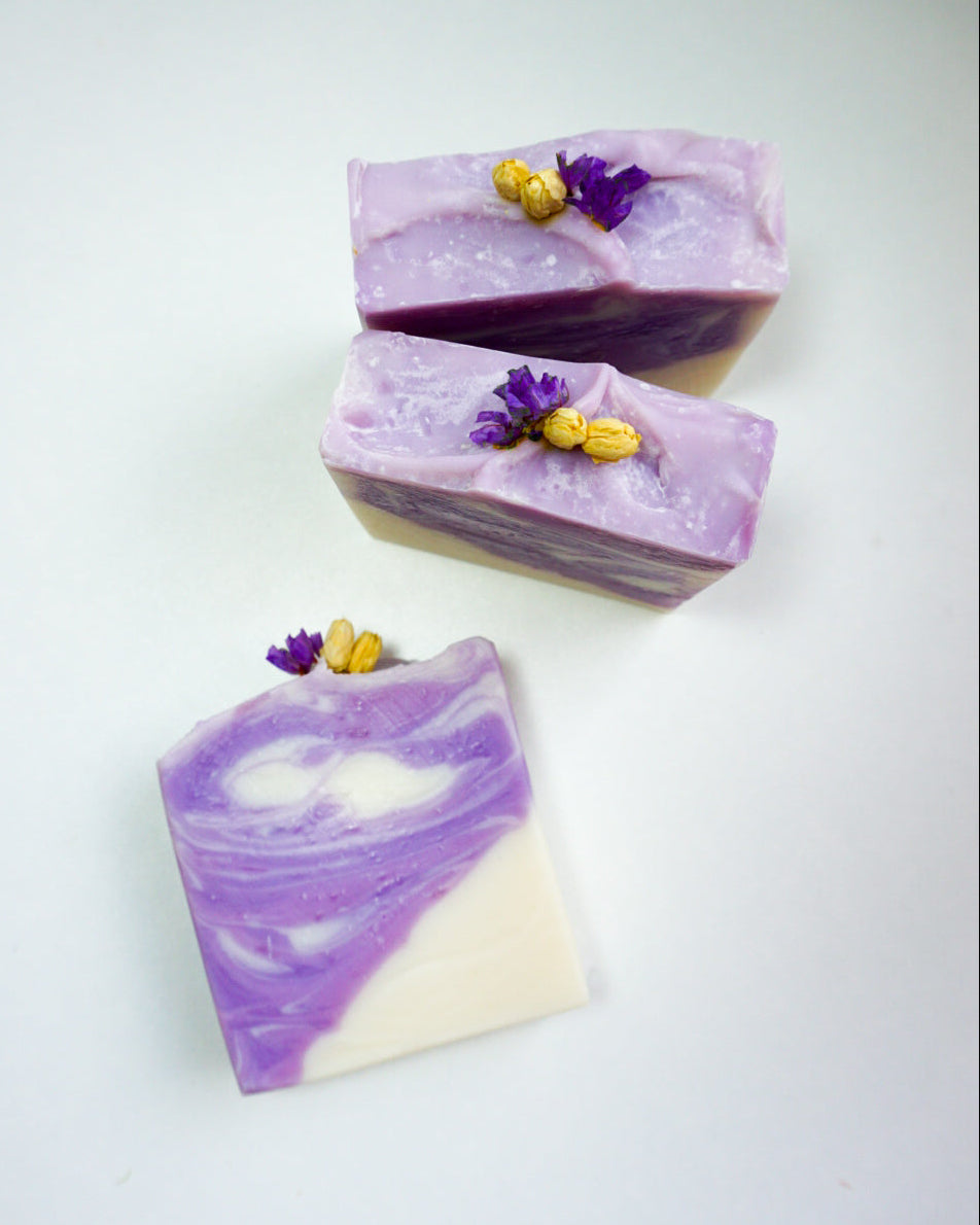 Three bars of purple and white soap with yellow and purple flowers on a light gray background