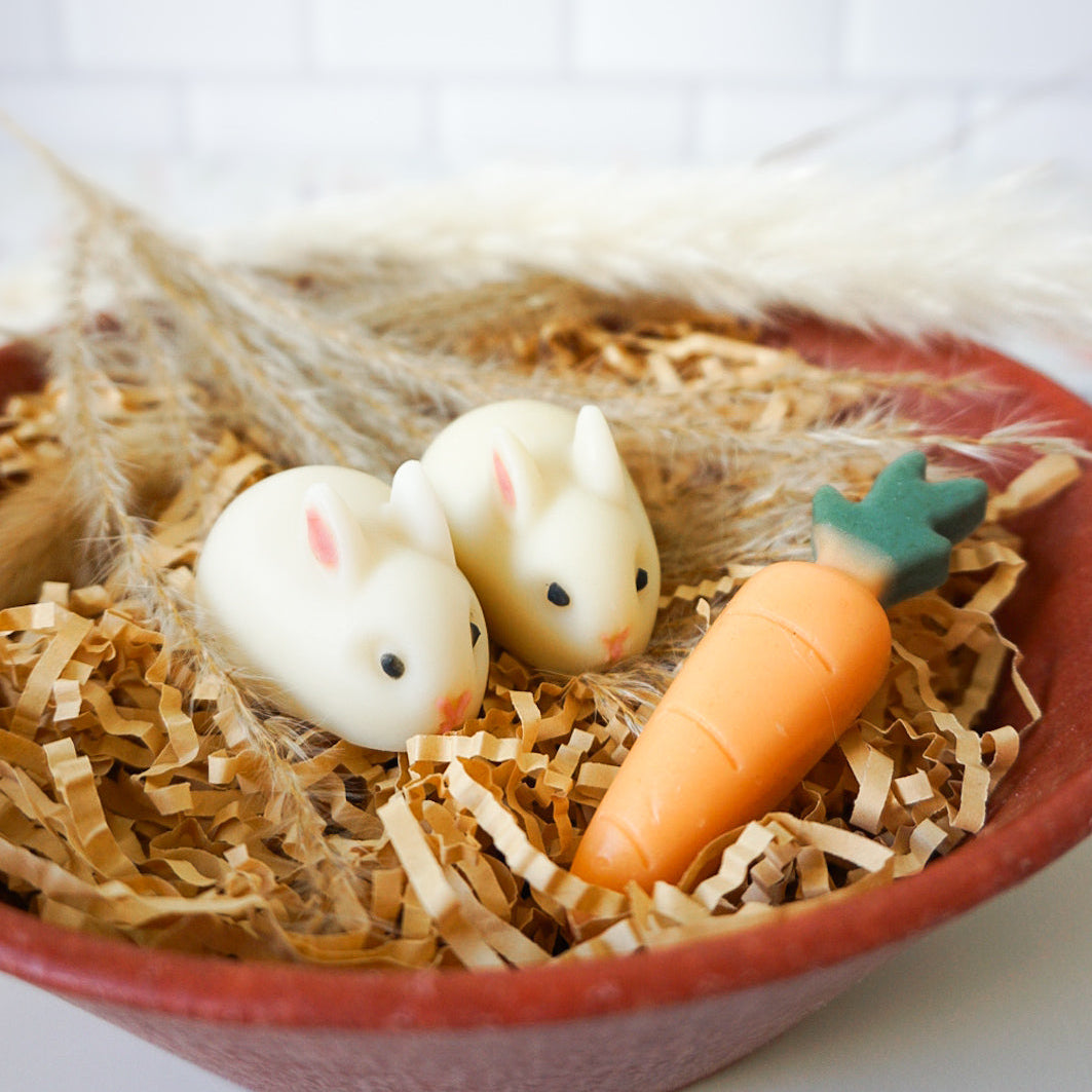 Two rabbit-shaped  soap and a carrot-shaped soap in a nest of straw on a white background
