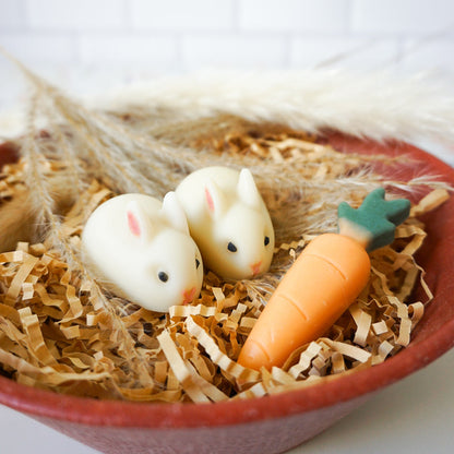 Two rabbit-shaped  soap and a carrot-shaped soap in a nest of straw on a white background