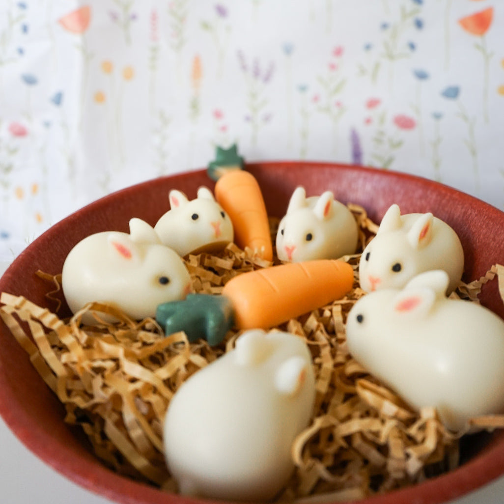 White rabbit-shaped soaps with carrot decorations in a red bowl on a colorful background