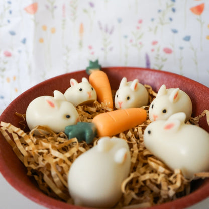 White rabbit-shaped soaps with carrot decorations in a red bowl on a colorful background