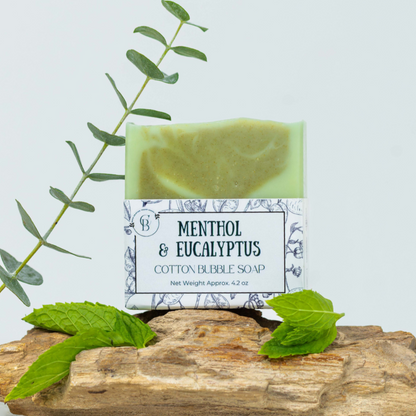 Bar of soap labeled 'Menthol & Eucalyptus' on a wooden block with green leaves.