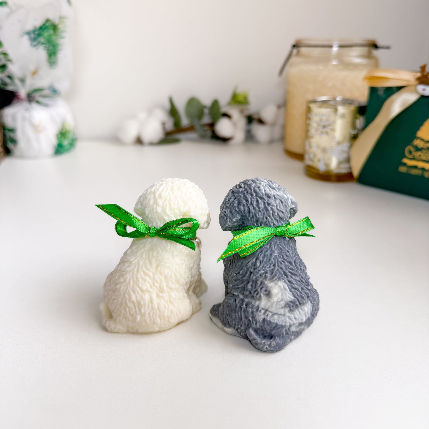 Two small dog figurine soaps, one white and one gray, with green ribbons on a white surface.