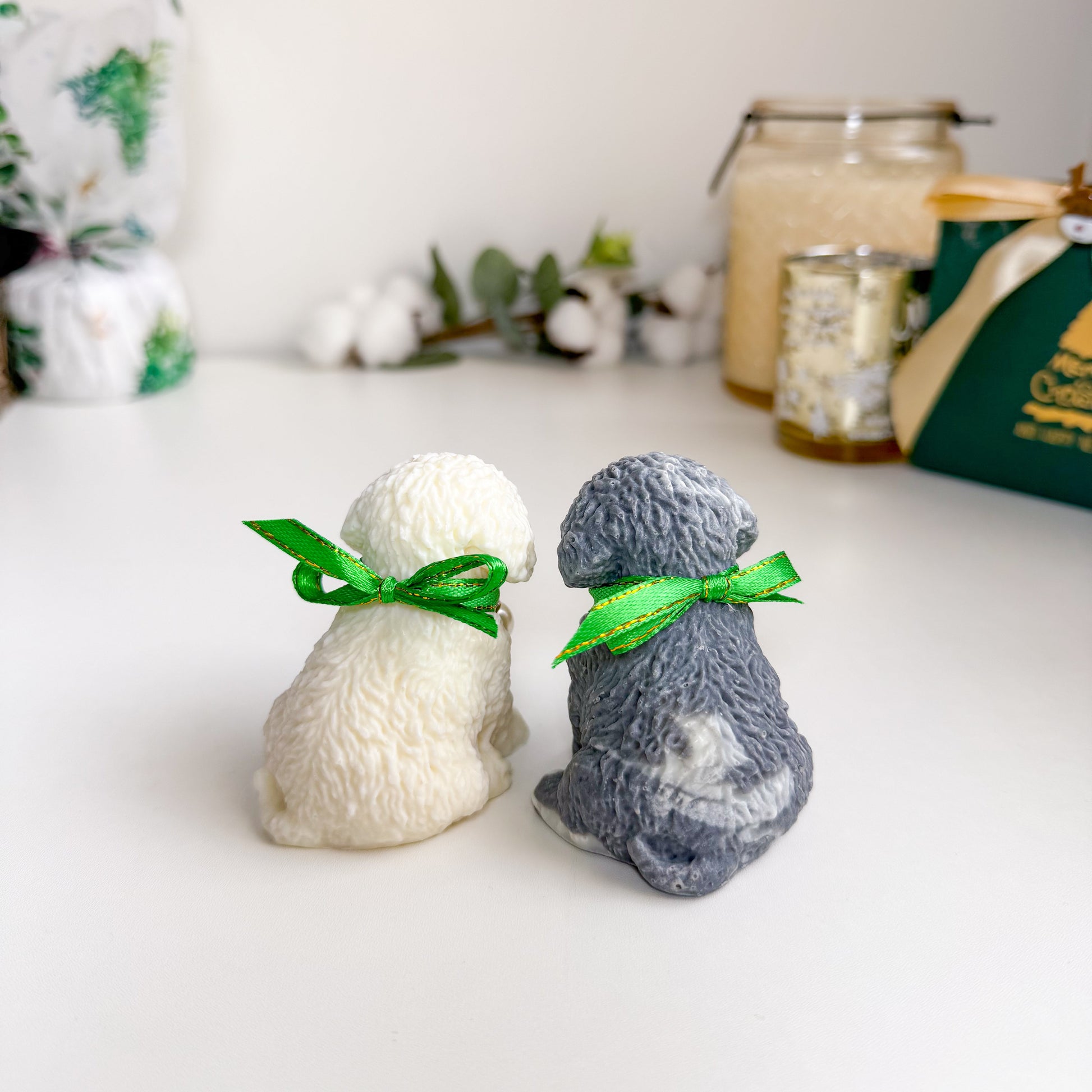 Two small dog figurine soaps, one white and one gray, with green ribbons on a white surface.
