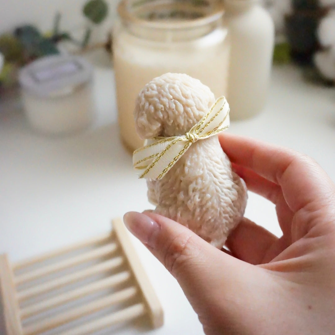 Hand holding a small decorative dog figurine soap with a gold ribbon on a blurred background.