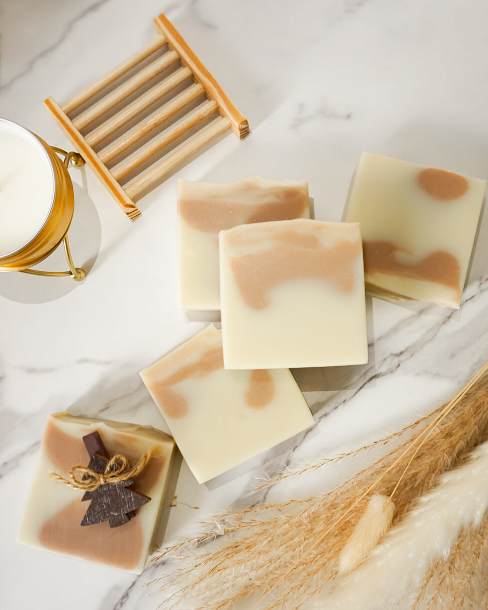 Handmade soap bars with a wooden soap dish on a marble surface