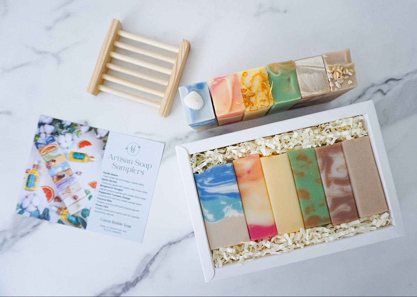 Set of colorful soap bars in a box with a wooden soap dish and leaflet on a marble surface