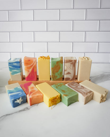 Assorted colorful soap bars displayed on a wooden stand against a white tiled wall.