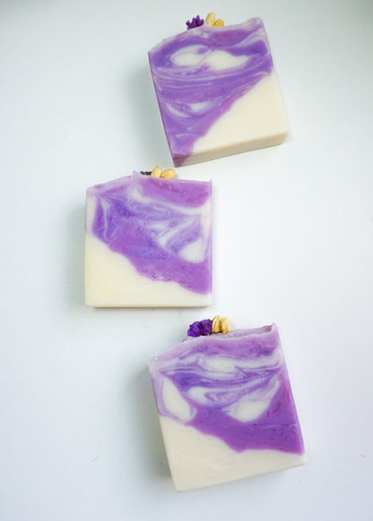 Three bars of purple and white soap with lavender buds on a light gray background