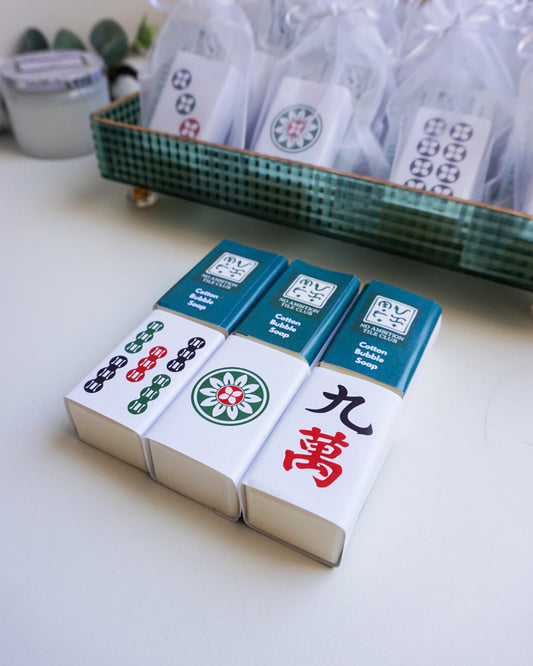 Set of Chinese mahjong tiles with green and white packaging on a light surface.